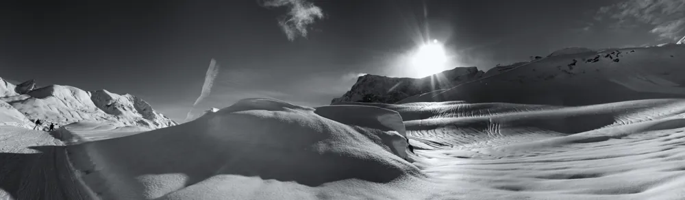 Schneeverwehungen und Berggipfel im Gegenlicht.