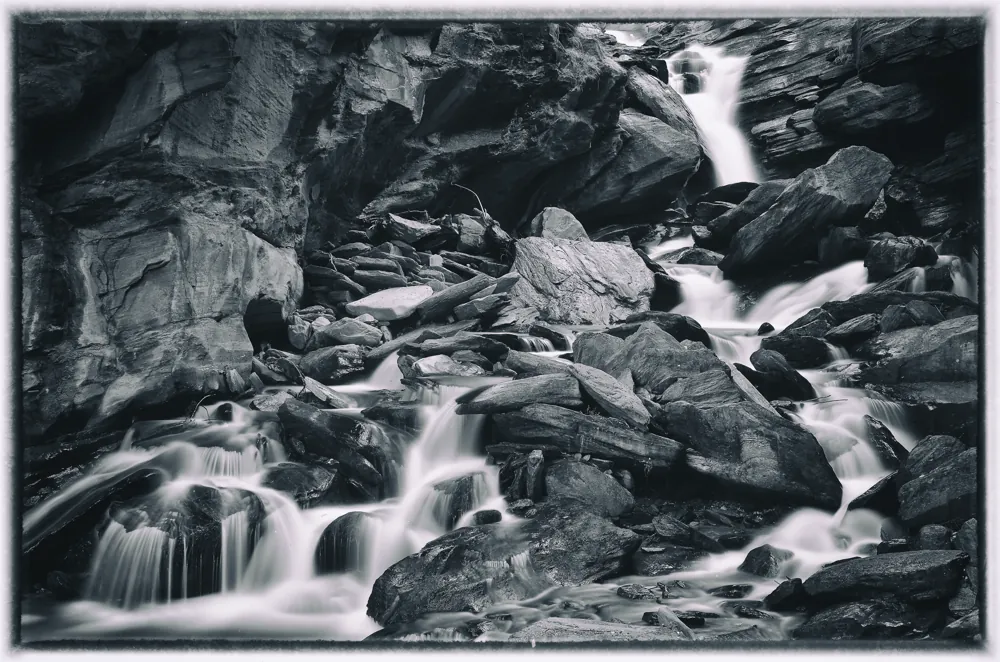 Fließendes Wasser zwischen dunklen Felsen in Schwarzweiß.